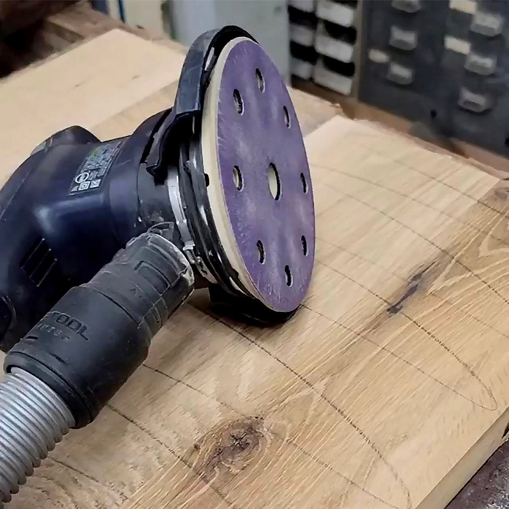 Purple ceramic 9-hole sanding disc fitted to a random orbit sander on a live edge wood slab