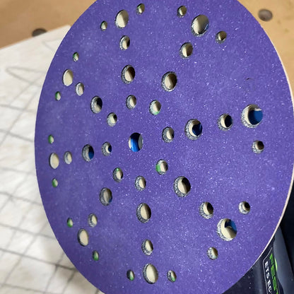Purple ceramic 6 inch multi-hole sanding disc on a sander pad with the holes aligned for dust extraction