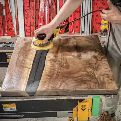 Woodworker buffing hard wax oil into a walnut slab using a random orbit sander and finishing pad